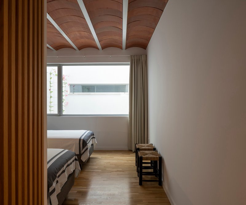 Bedroom with curved timber ceiling beams and horizontal window overlooking neighboring rooftops