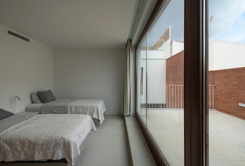 Bedroom with floor-to-ceiling glazing opening onto a private terrace overlooking adjacent brick walls
