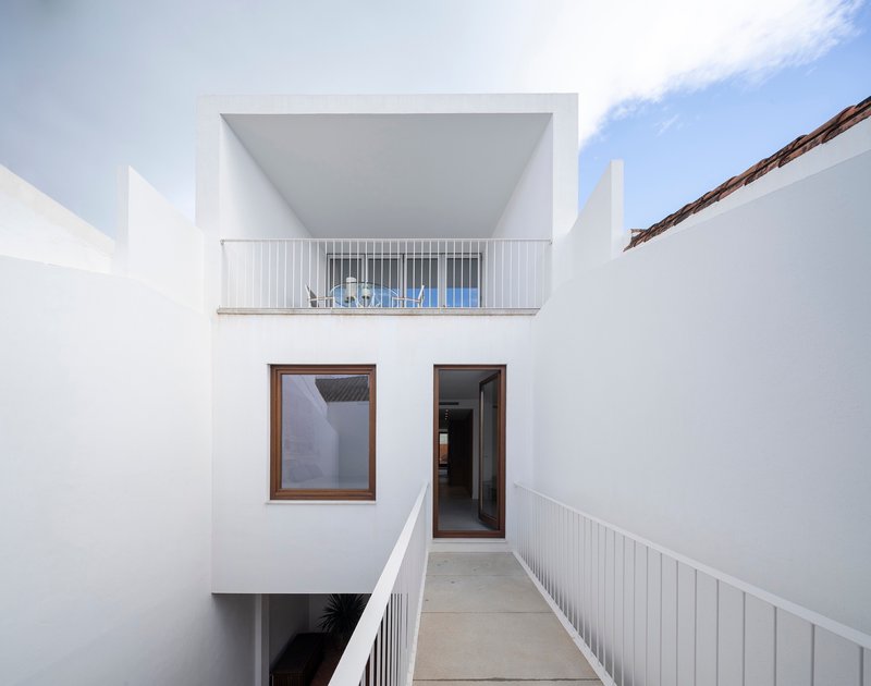 White rendered courtyard passage with upper balcony and metal railings under bright midday sun