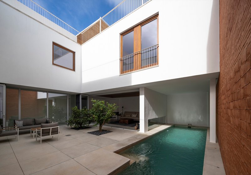 Courtyard pool with planted tree bed, white columns and brick wall in afternoon shadow