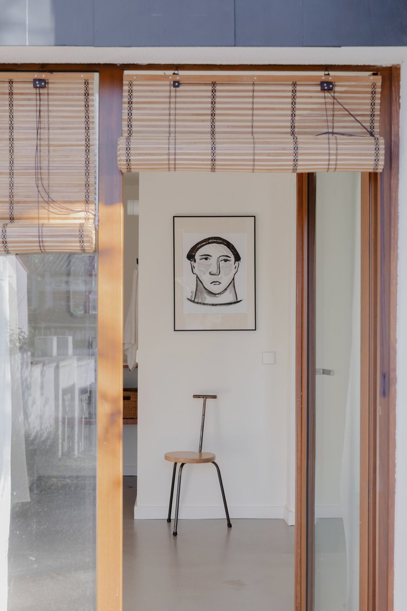 Timber framed doorway with woven bamboo blind leading into a room with a framed portrait and chair