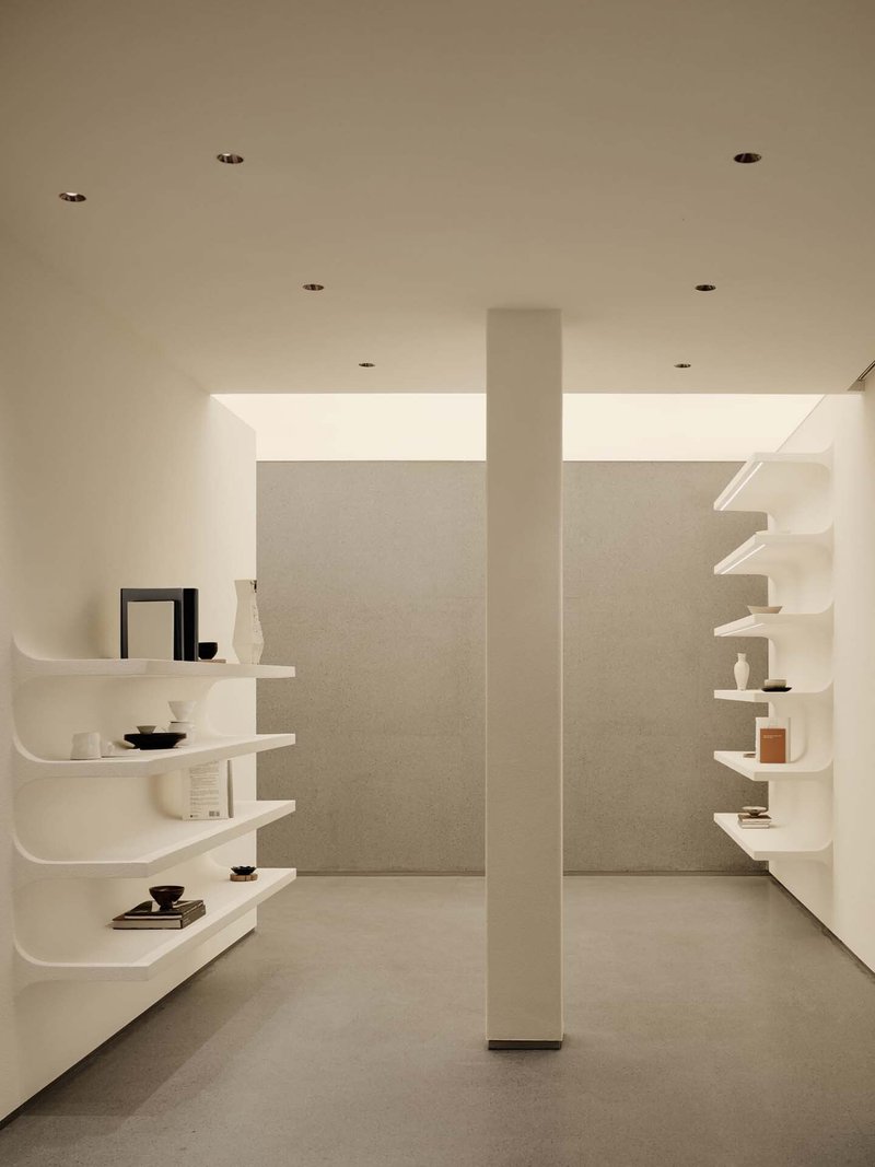 Curved white floating shelves displaying ceramics and books flanking a central column with clerestory windows above