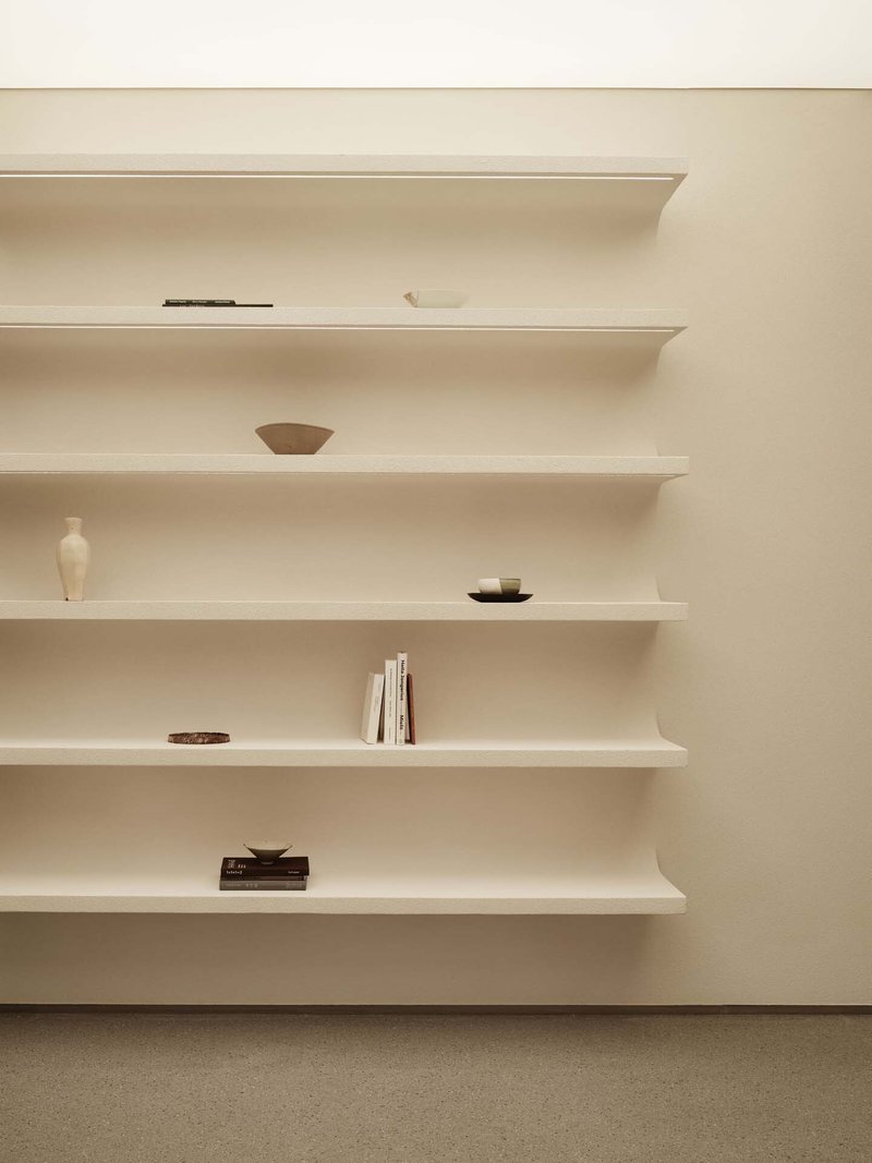 Close-up of rounded white wall-mounted shelves holding sparsely arranged pottery and stacked books