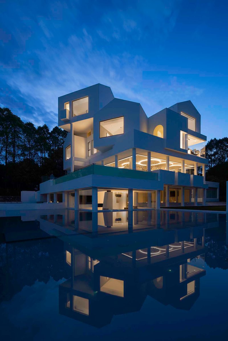 Sculptural white facade reflected in still water at twilight with glowing interior lights