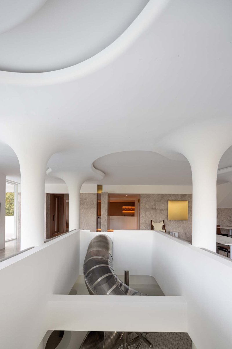 Interior view through sculptural white ceiling opening revealing upper level with stone walls and timber doors