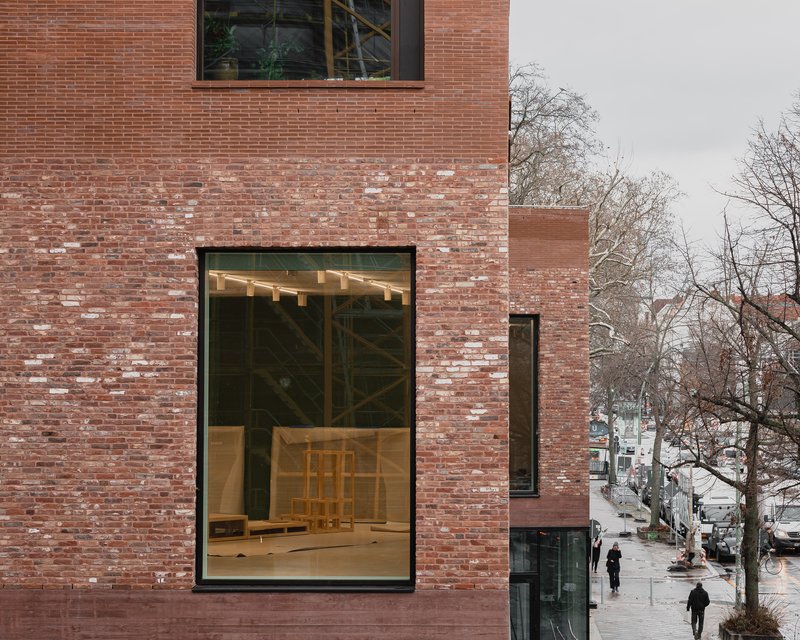 Tall glazed opening in the brick facade revealing exposed timber structure and pedestrians below