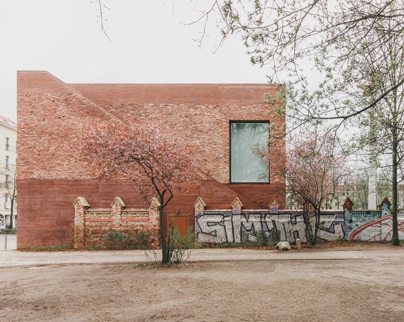 Rear facade showing red brick volumes and partial remnant wall with graffiti in autumn