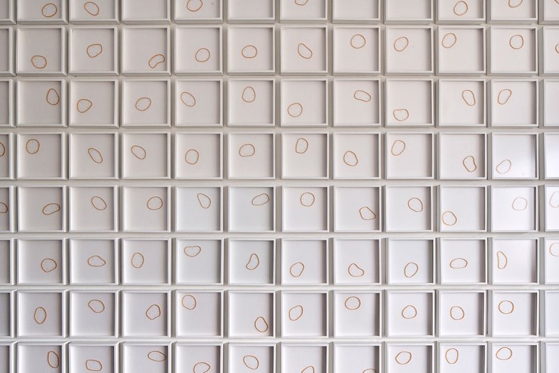 White grid wall panel with copper wire loops set into each recessed square cell
