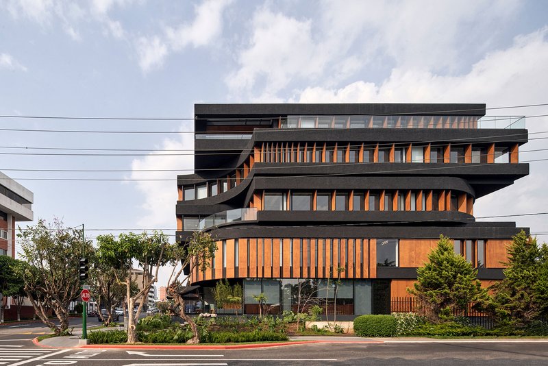 Stacked facade with dark concrete slabs and vertical timber screening viewed from the street under cloudy skies