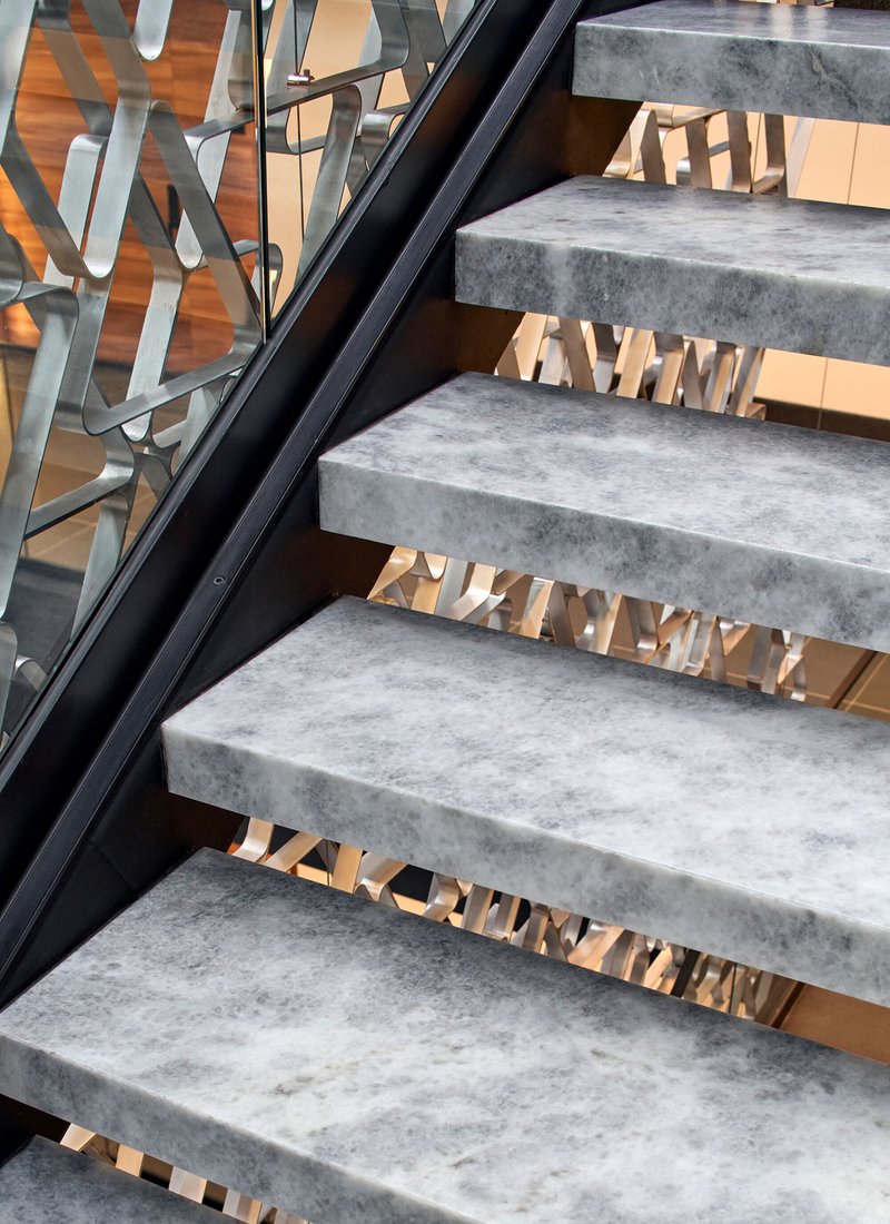 Concrete stair treads with black steel stringers and brass textured risers behind a glass balustrade