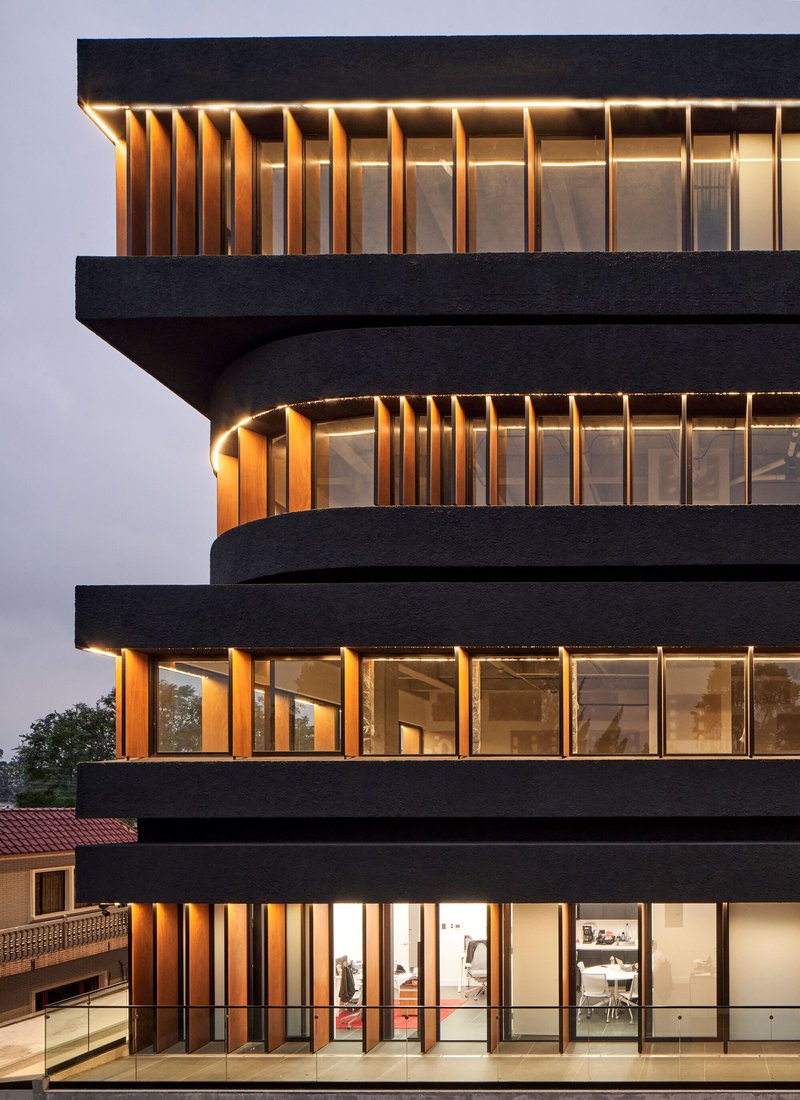 Detail of the cantilevered floor slabs with vertical timber fins between dark horizontal bands at dusk