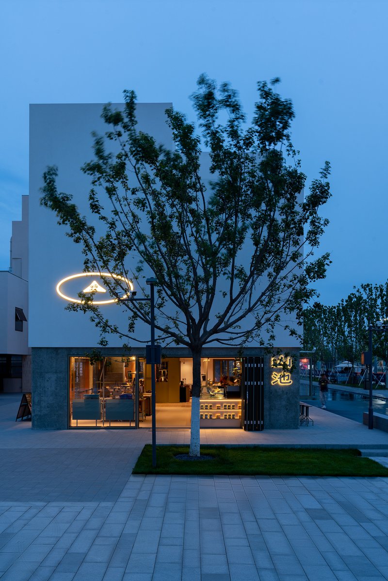 Street view of a white facade with circular streetlight and tree silhouetted against the blue hour sky