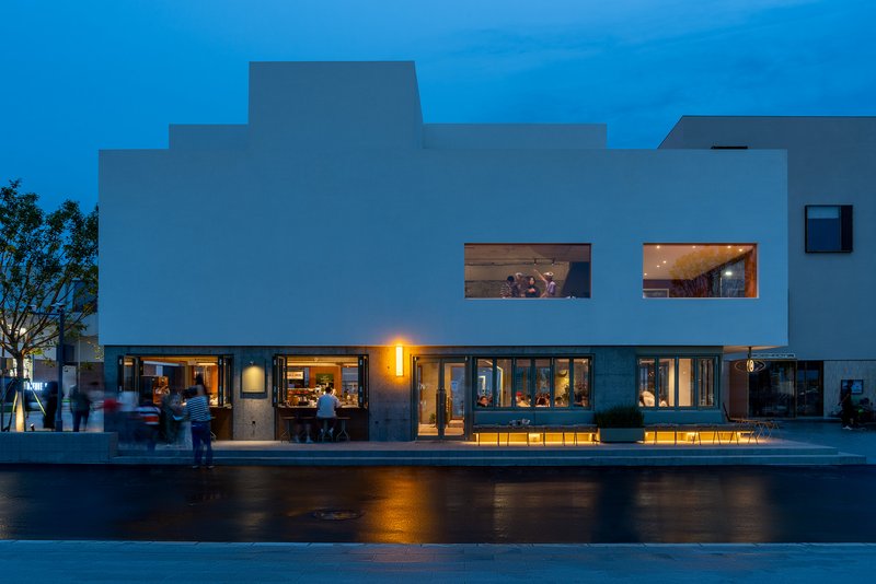 White stepped facade with horizontal window openings and warm interior lighting at twilight
