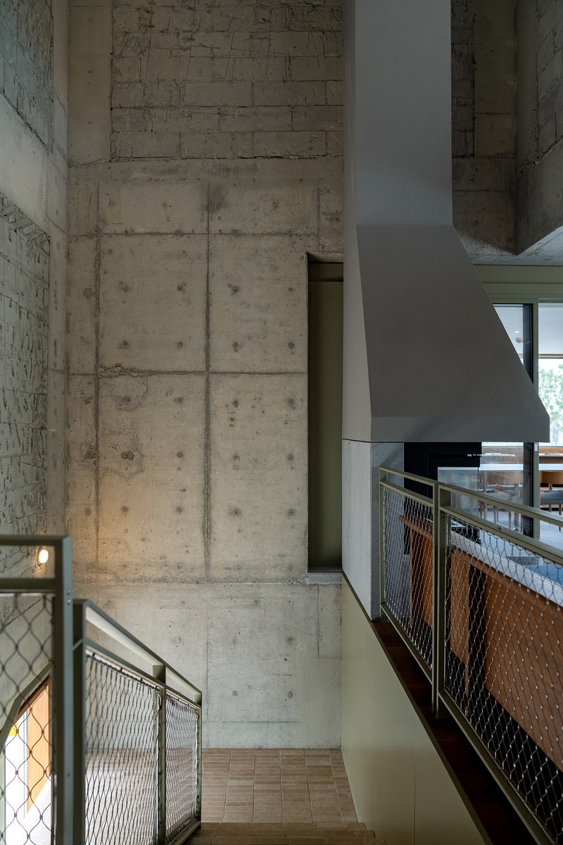 Double-height space with exposed concrete walls and metal mesh balustrade in afternoon light