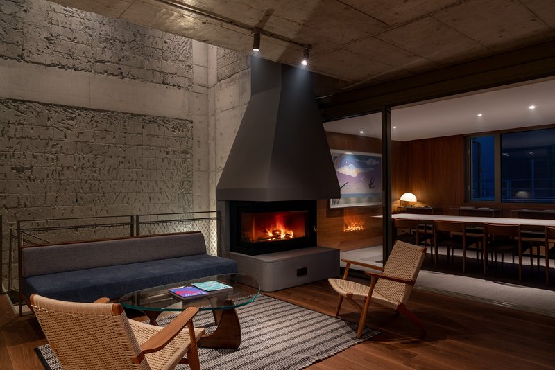 Double-height living room with exposed concrete walls, suspended metal fireplace, and dining area visible beyond