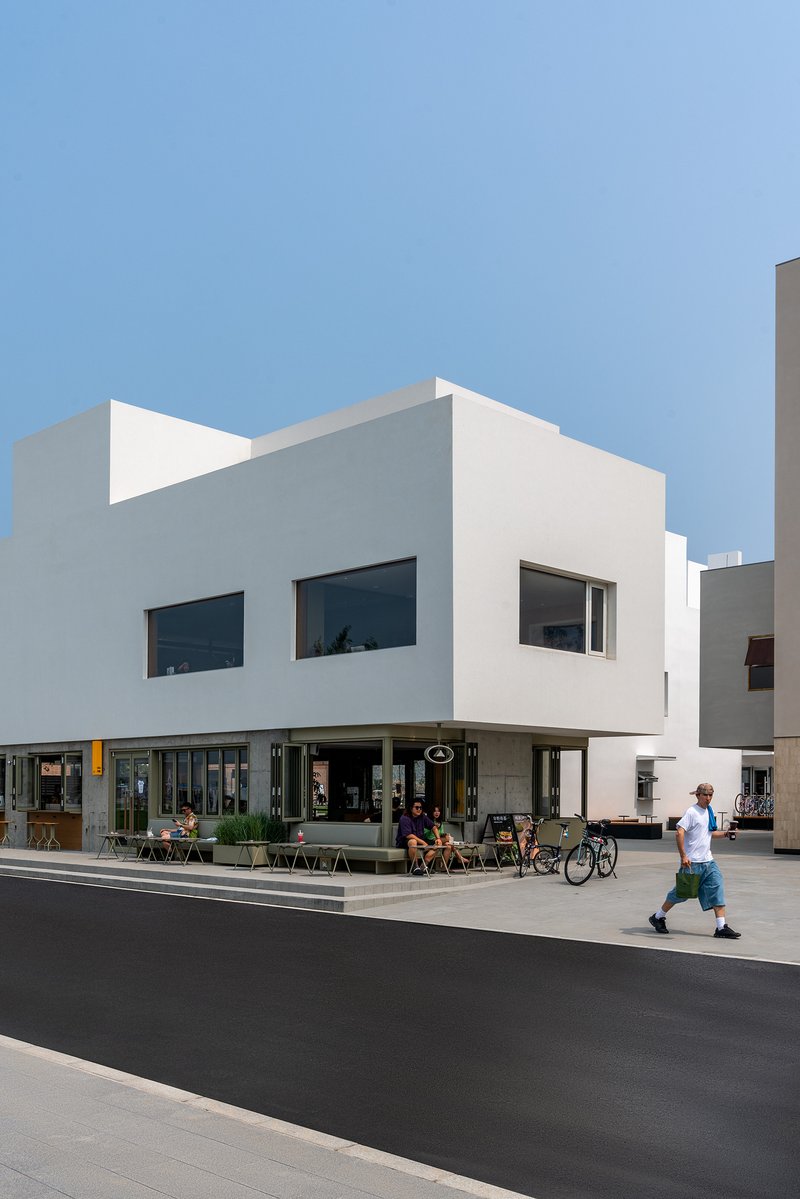 White rendered facade with ground-floor cafe and pedestrians passing on the street