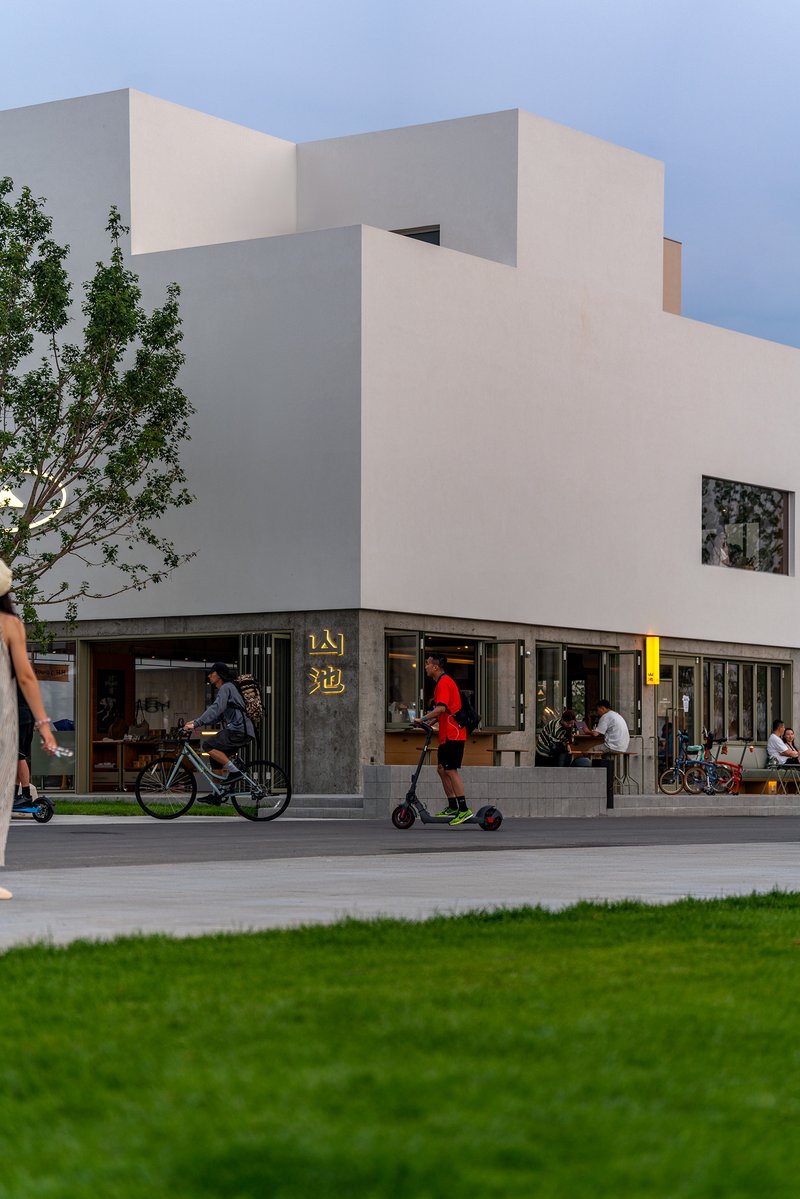 Street view of stacked white volumes above ground-floor retail with cyclists and pedestrians