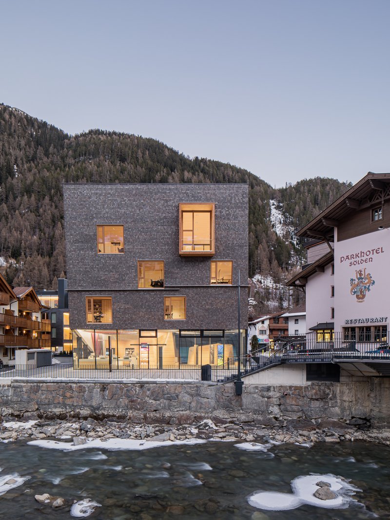 Dark slate shingle facade with illuminated windows overlooking a rushing river at dusk