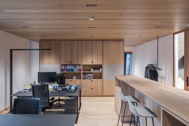 Open office area with timber cabinetry, work desks and wood plank ceiling with recessed lighting