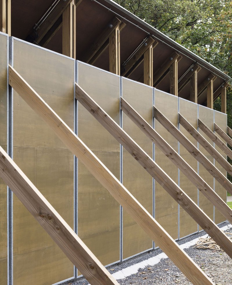 Diagonal timber bracing with metal tension rods supporting plywood wall panels under exposed rafters