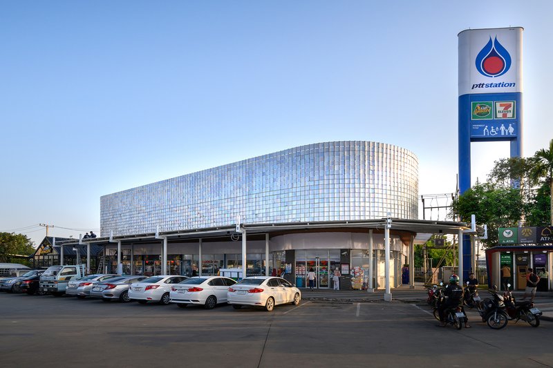 Curved facade with vertical glass panel cladding atop a ground-level service station under a clear sky