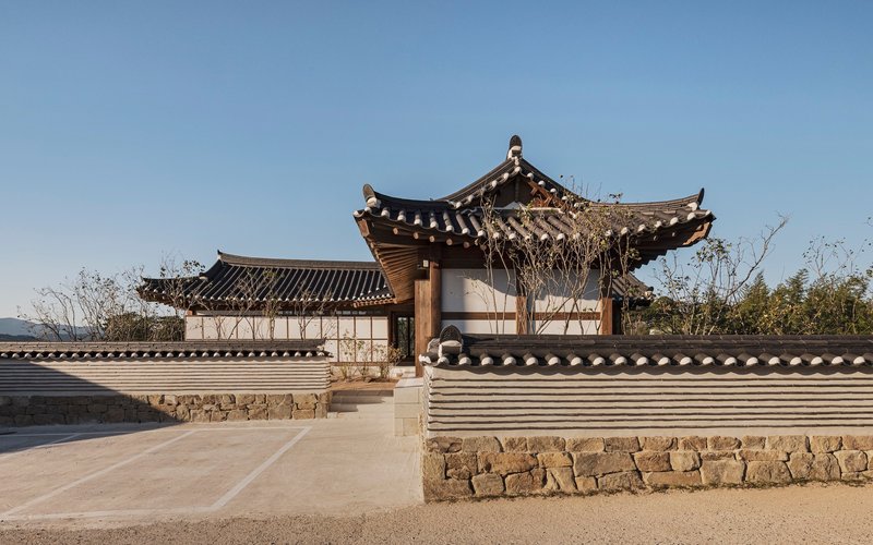 Courtyard entrance with traditional tiled roofs atop stone walls and white plaster under a clear sky