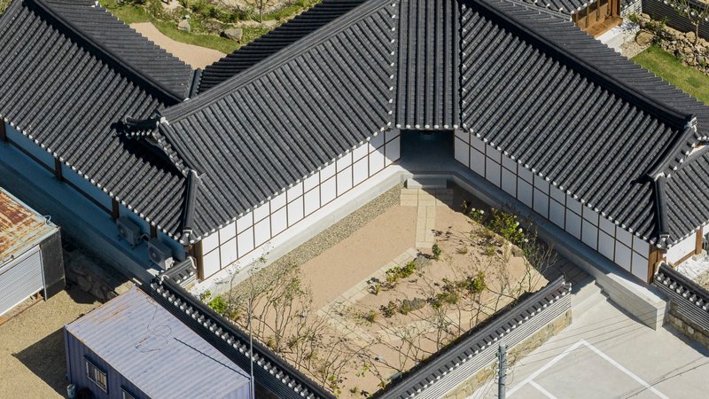 Aerial view of the tiled roofs enclosing a gravel courtyard with young trees and plantings