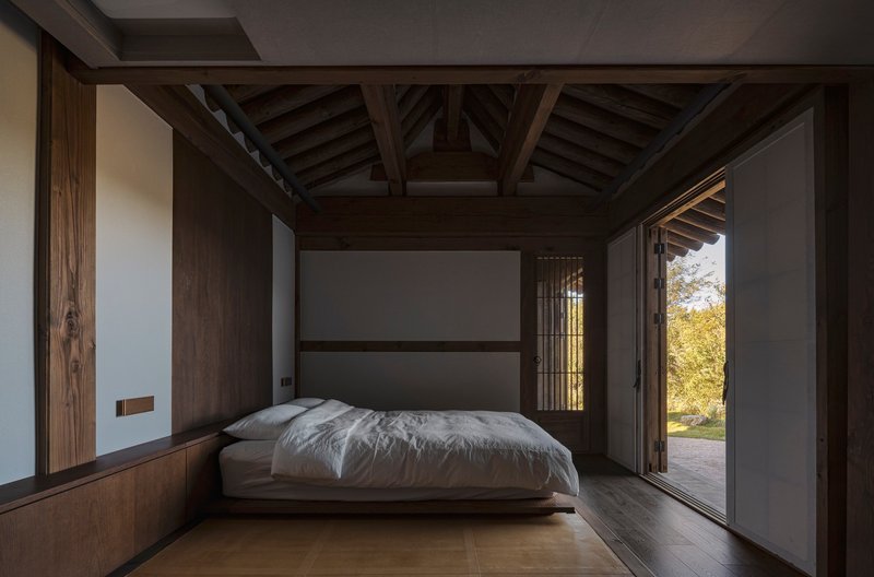 Bedroom with exposed timber structure and sliding doors opening to the exterior garden