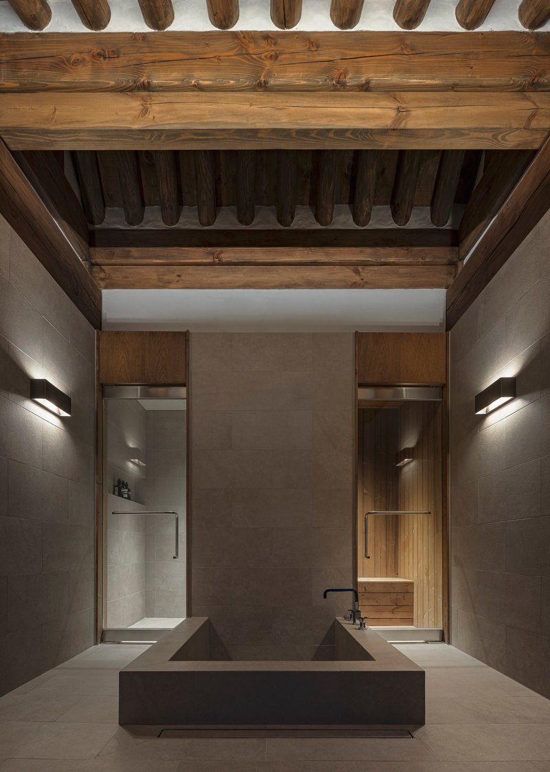 Bathroom with double concrete basin under exposed timber ceiling beams and flanking wall sconces