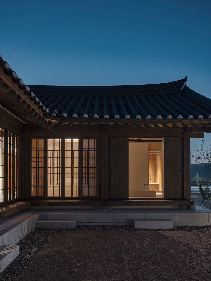 Timber pavilion with curved tiled roof and translucent gridded screens illuminated at dusk