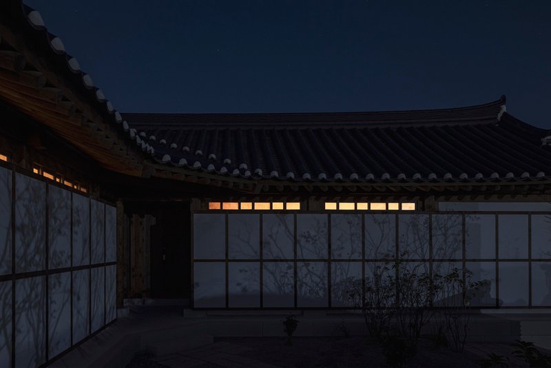 Courtyard facade with translucent panels and illuminated clerestory windows under sweeping tiled eaves at dusk