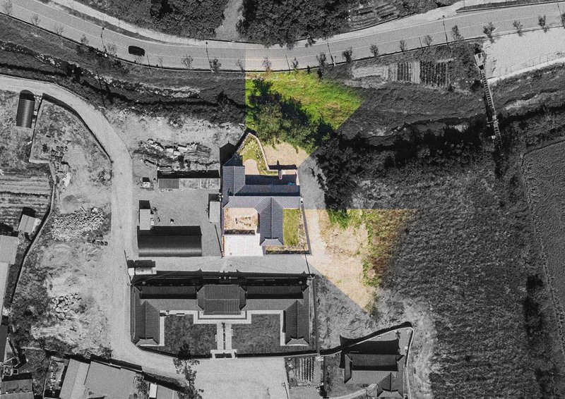 Aerial view of a cross-shaped compound with dark roofs and green courtyard spaces between surrounding agricultural fields
