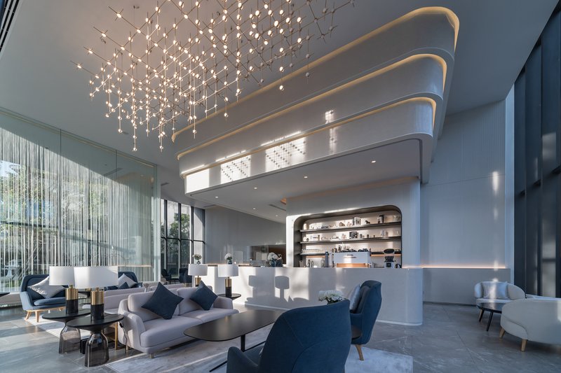 Double-height lobby with curved ceiling coves, cascading light installation, and curved reception desk below mezzanine