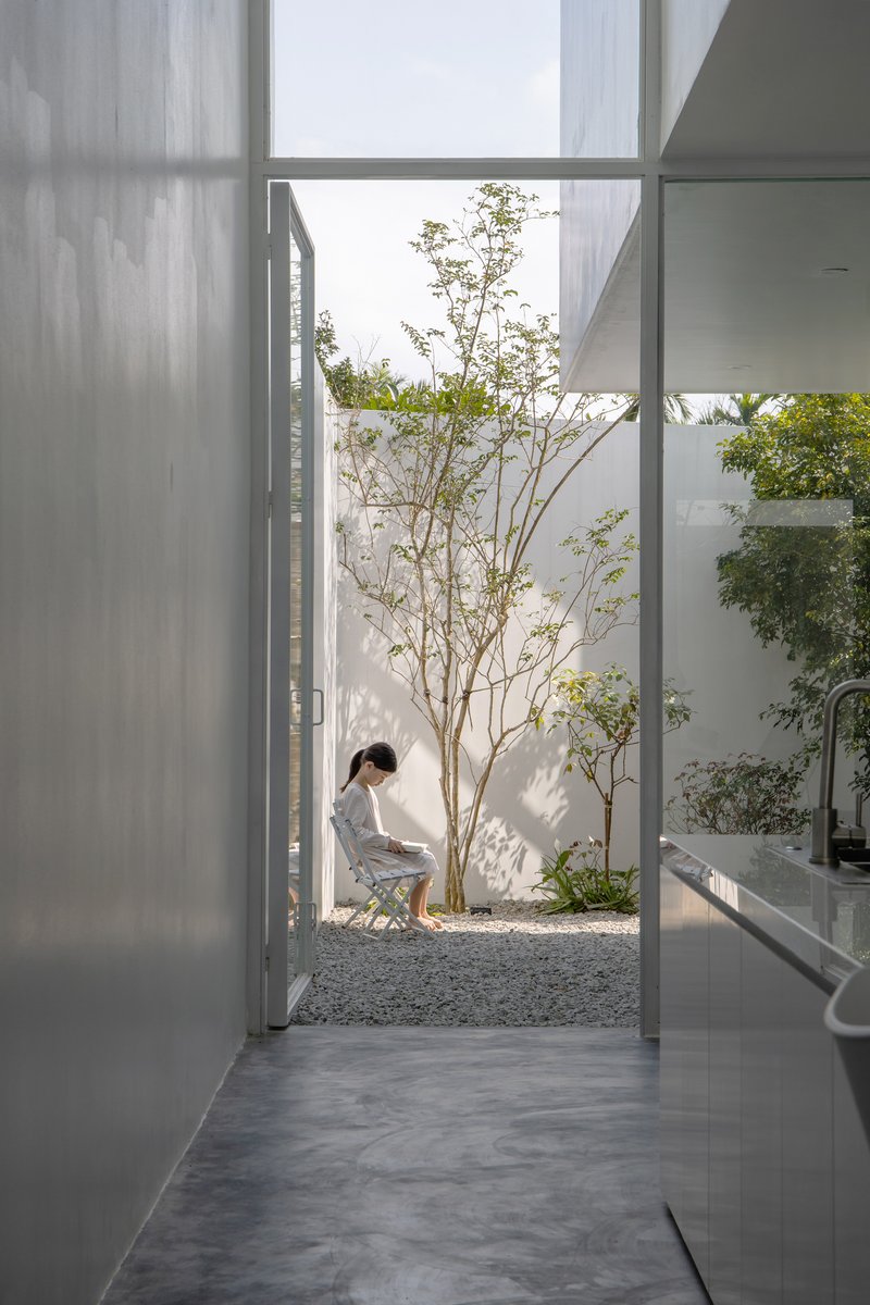 View from a bathroom through sheer curtains to a gravel courtyard where a person sits