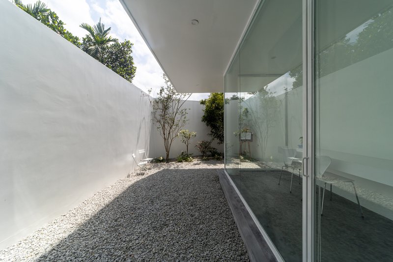 Enclosed courtyard with gravel floor and floor-to-ceiling glass wall under partial shade