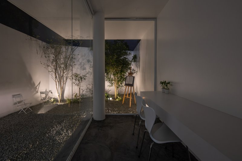 Interior view looking through glass walls to a gravel courtyard with planted trees at dusk