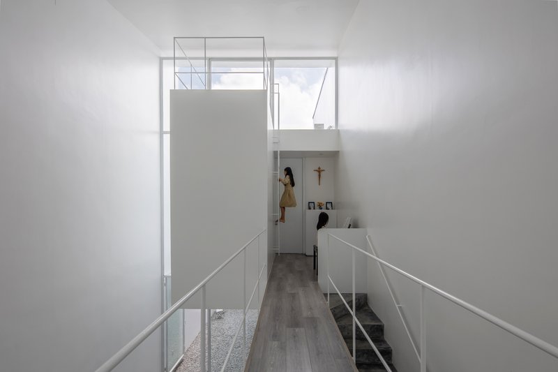 Double-height interior space with a bridge and figure on upper level illuminated by skylight
