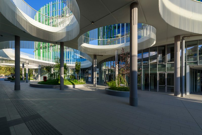 Covered entrance plaza with cylindrical columns, curved canopy and planted beds beneath a blue sky