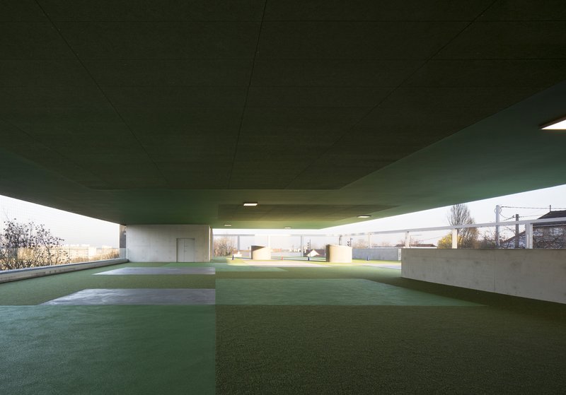 View beneath the green cantilevered ceiling with concrete columns and artificial lawn at dusk