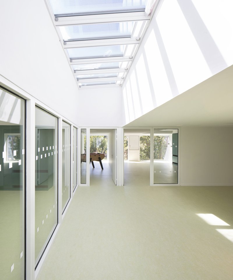 Skylit corridor with glazed walls connecting interior spaces with sunlight filtering through overhead louvers