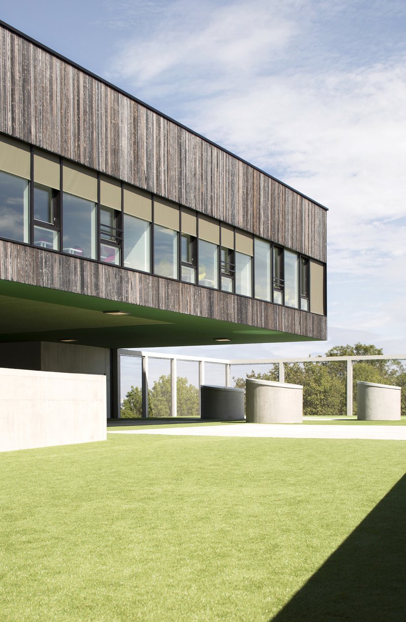 Cantilevered upper volume with vertical timber cladding and ribbon windows over green lawn