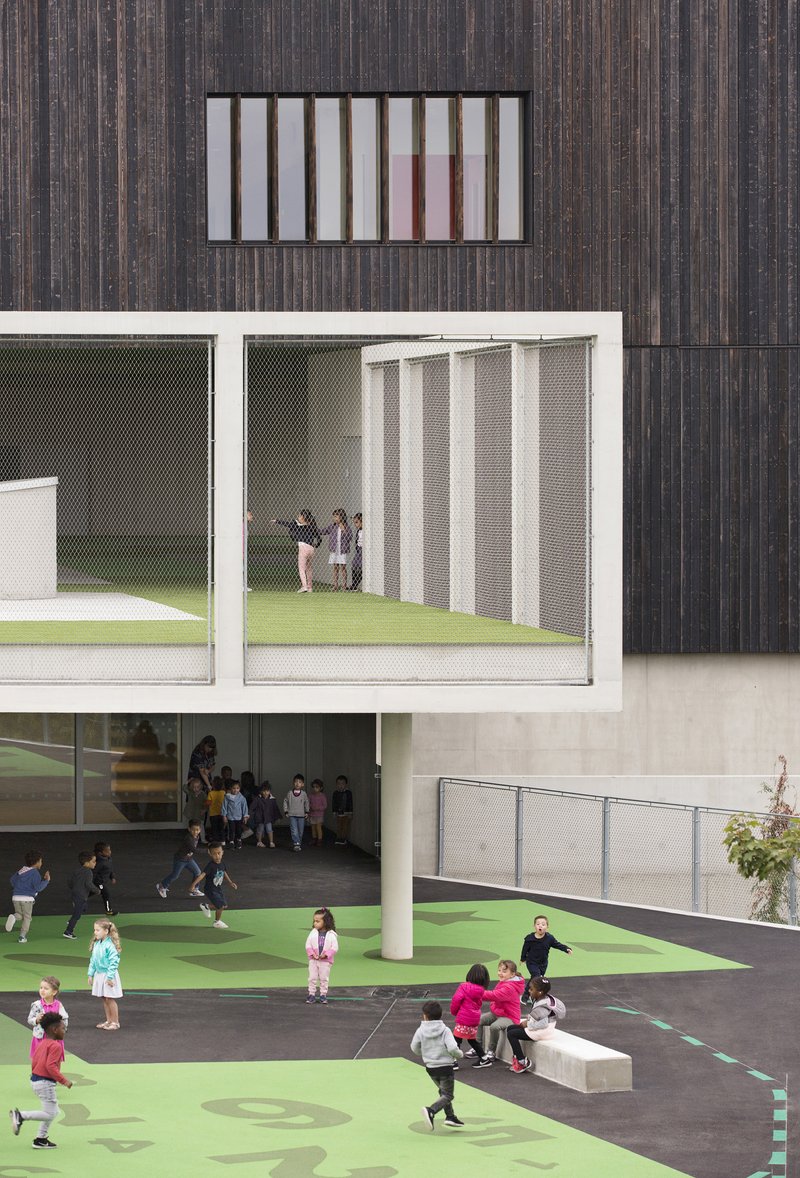 Courtyard with green play surface, mesh-screened balcony, and children gathering under cantilevered volumes