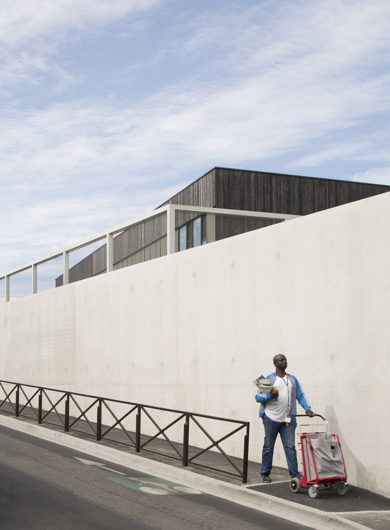 Delivery worker with cart passing along the street-level concrete wall below dark timber cladding