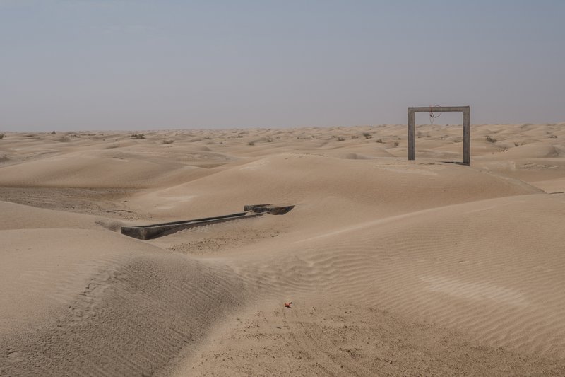 Concrete portal structure and partially buried water trough in windswept desert terrain under overcast sky