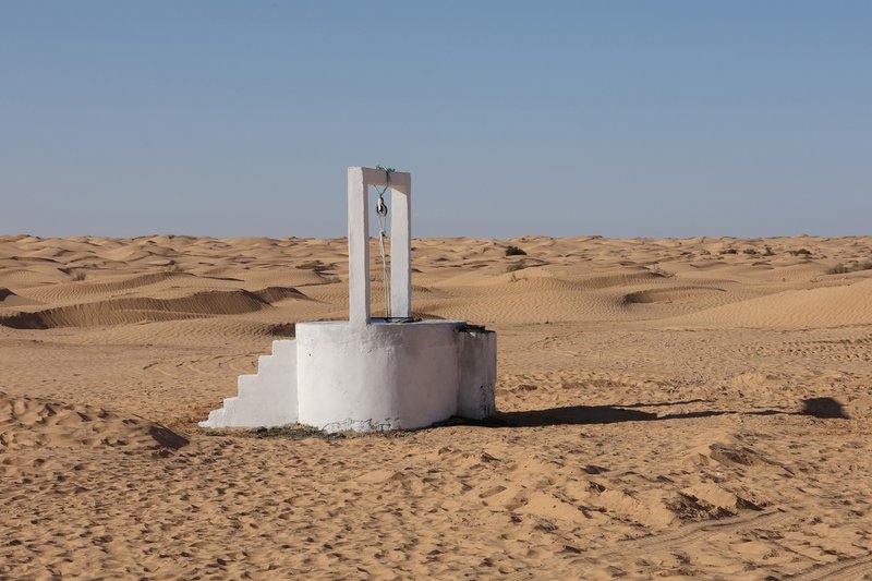 White plastered water well with vertical tower element rising from the sand dunes