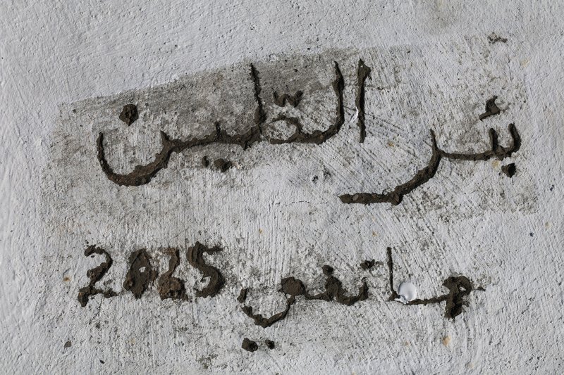 Close-up of Arabic script and numerals painted in dark pigment on weathered white plaster