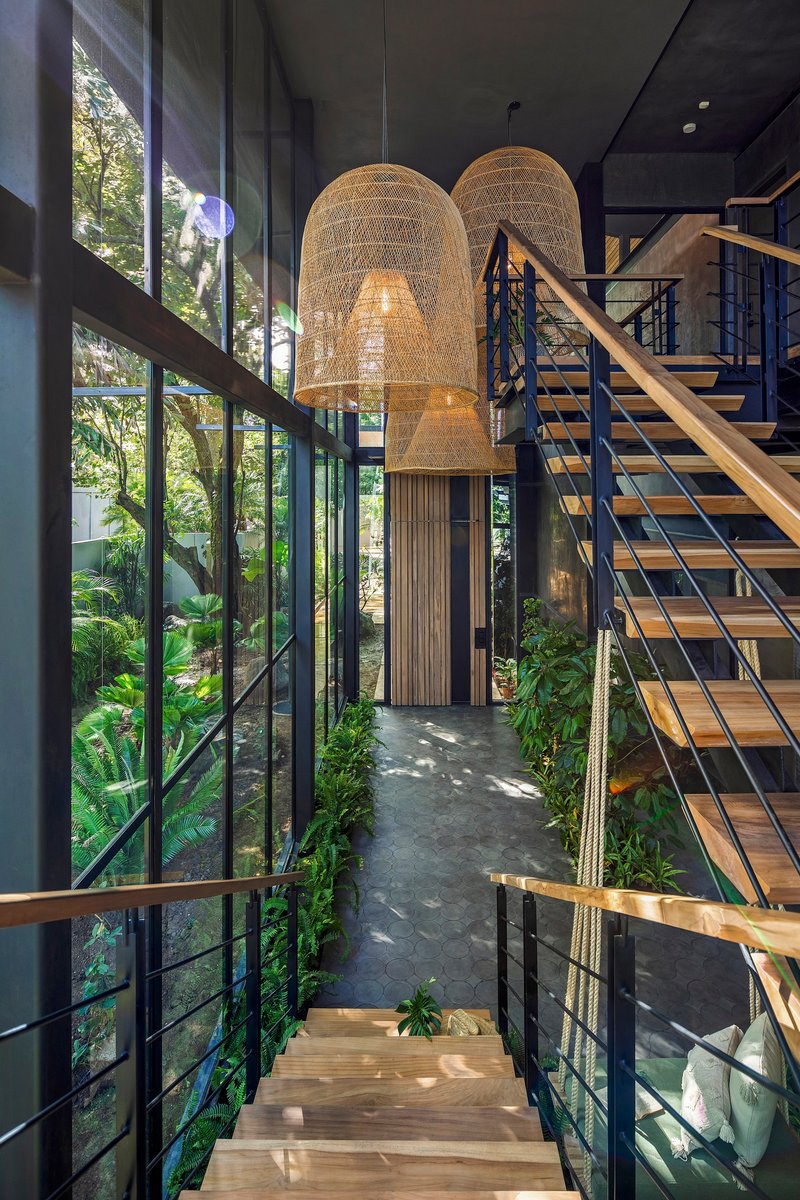 Double-height entry hall with woven pendant lights and metal staircase overlooking planted courtyard
