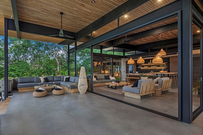 Covered terrace with steel frame opening to living spaces and garden at dusk