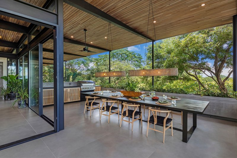 Outdoor dining terrace beneath a deep roof overhang with views to surrounding trees
