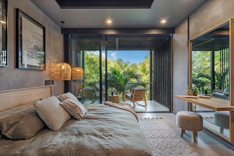 Bedroom with glass doors opening to a private balcony framed by foliage